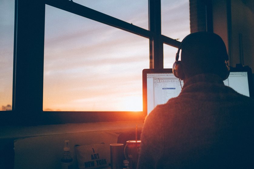 Man with headphones on sits at laptop watching sunset