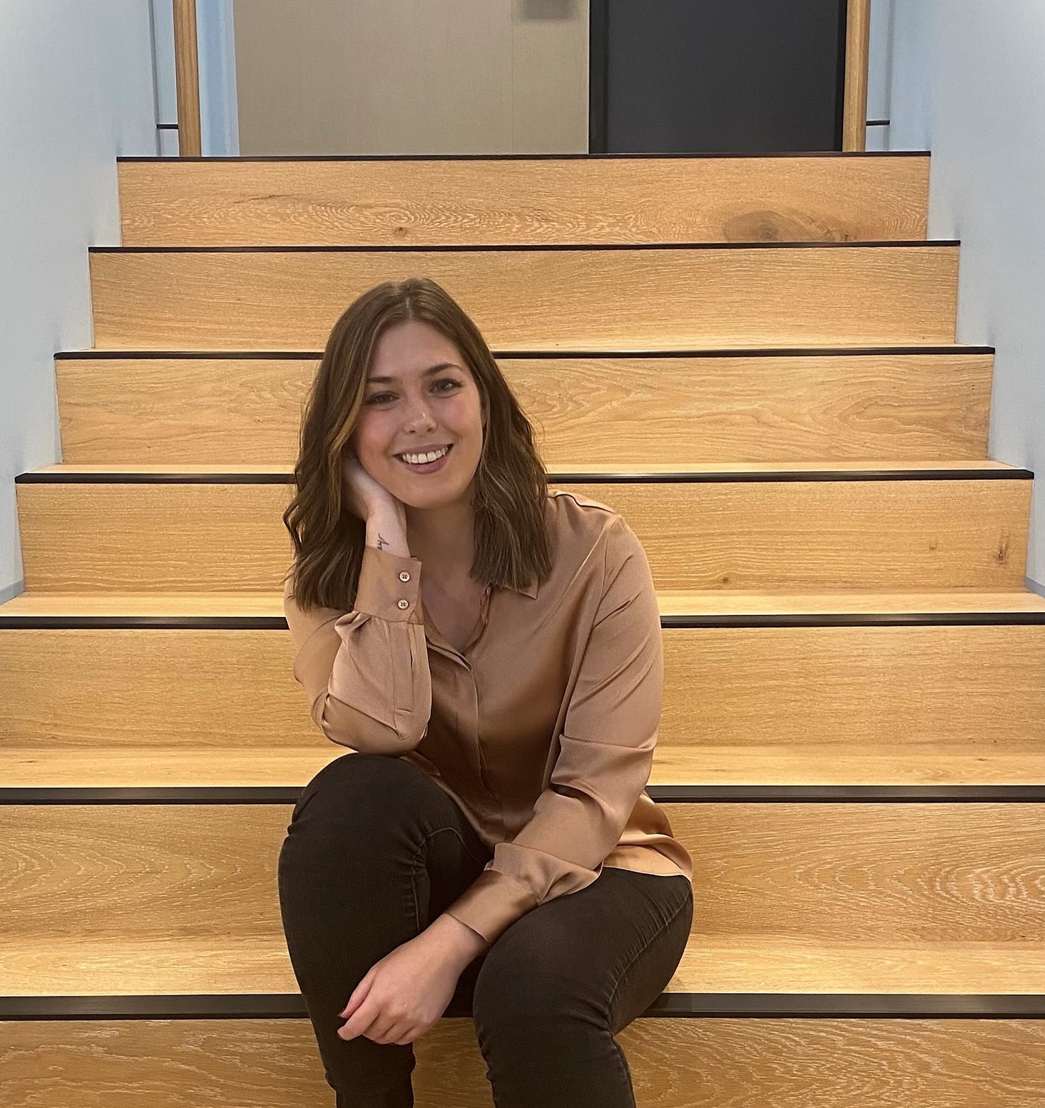 a young brunette woman in a tan blouse sits on a set of wooden stairs