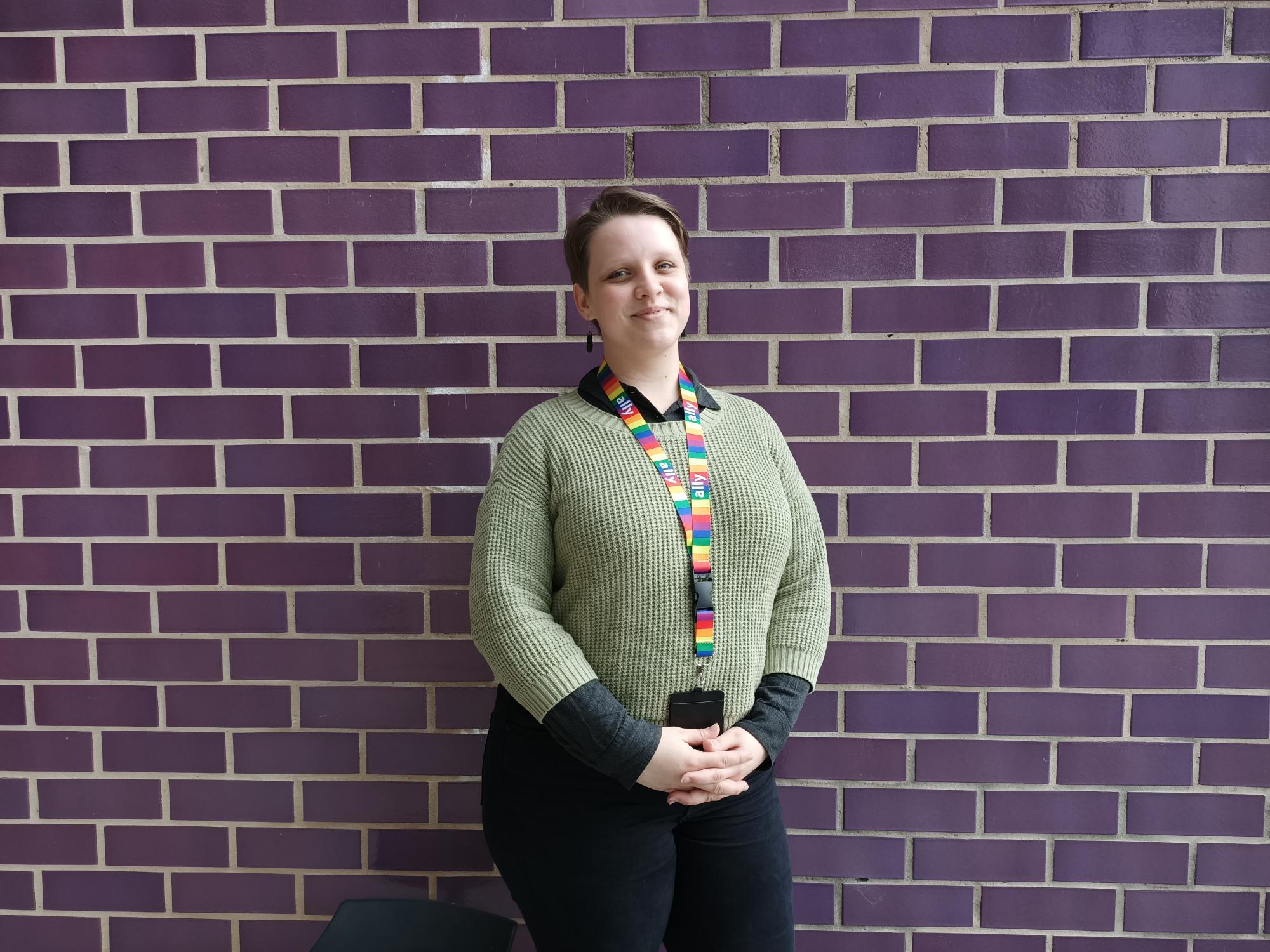 a young woman in a green sweater stands against a red brick wall